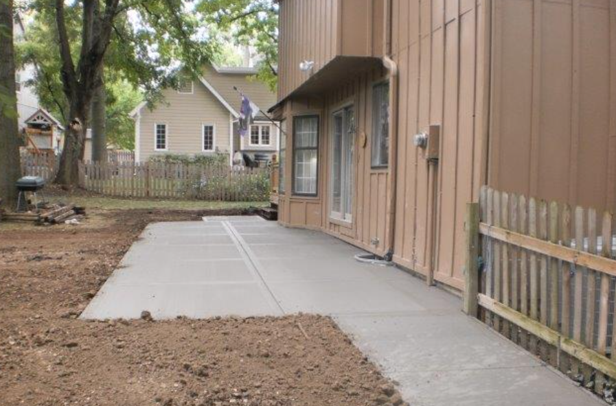 a concrete walkway leading to a house with a wooden fence