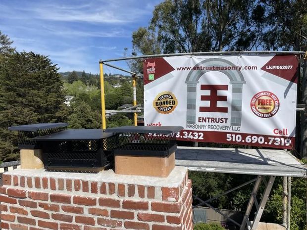 Chimney with new caps, scaffolding, and a business banner against a blue sky.