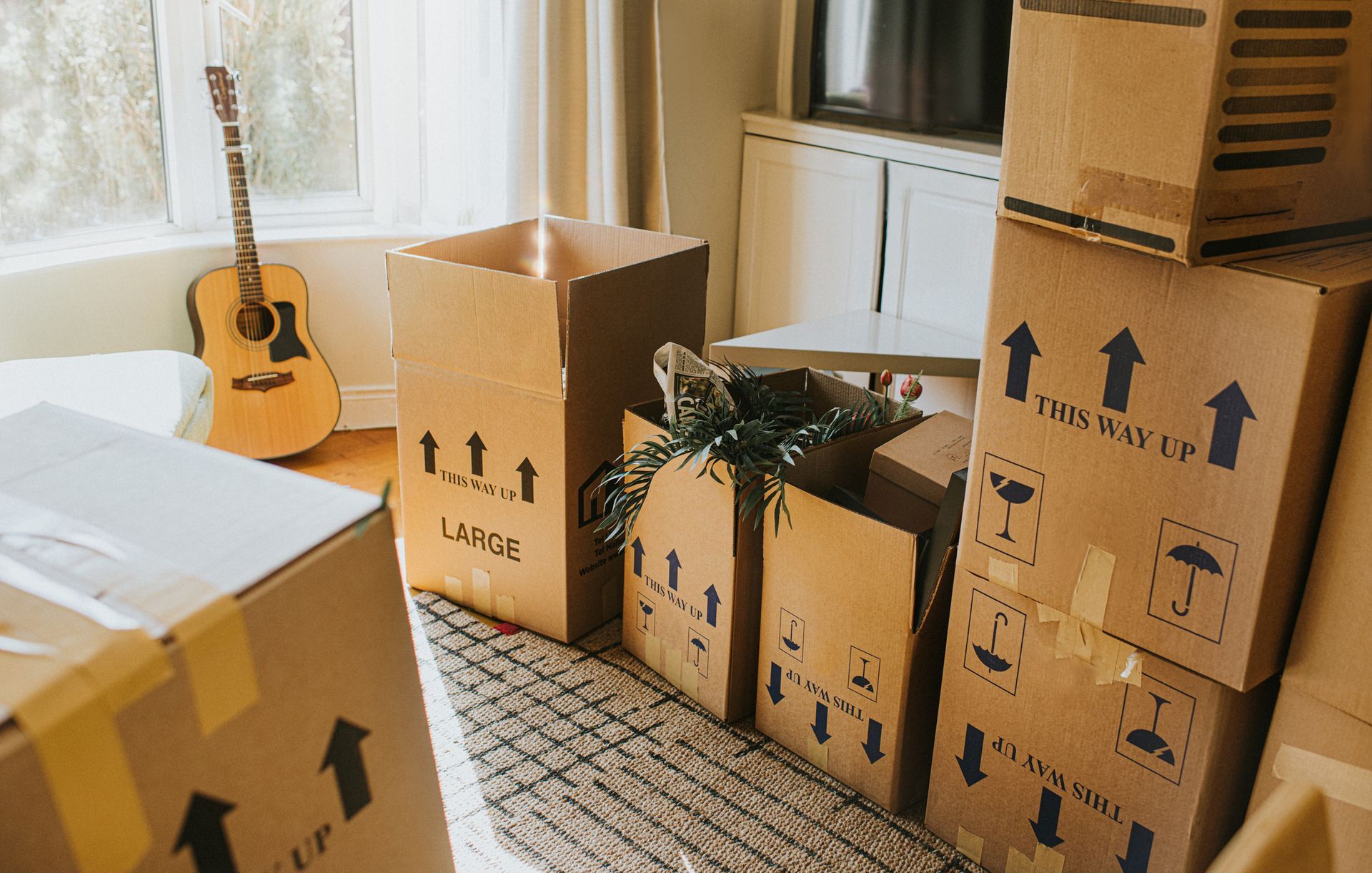 A living room filled with cardboard boxes and a guitar.