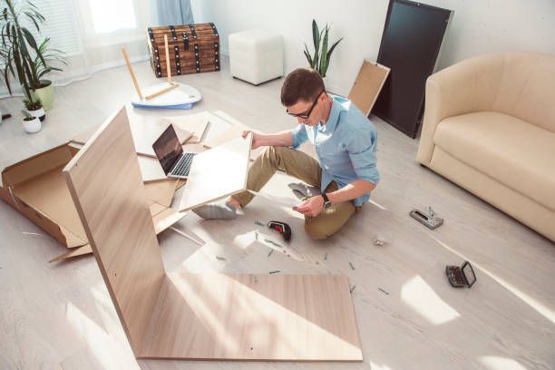 A man is sitting on the floor in a living room assembling a table.