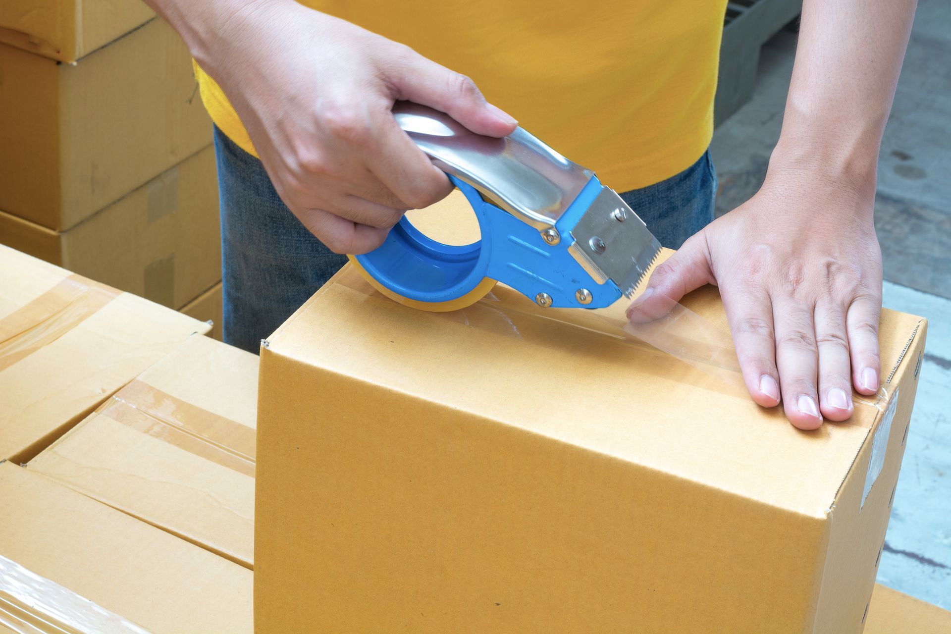 A person is taping a cardboard box with blue tape.