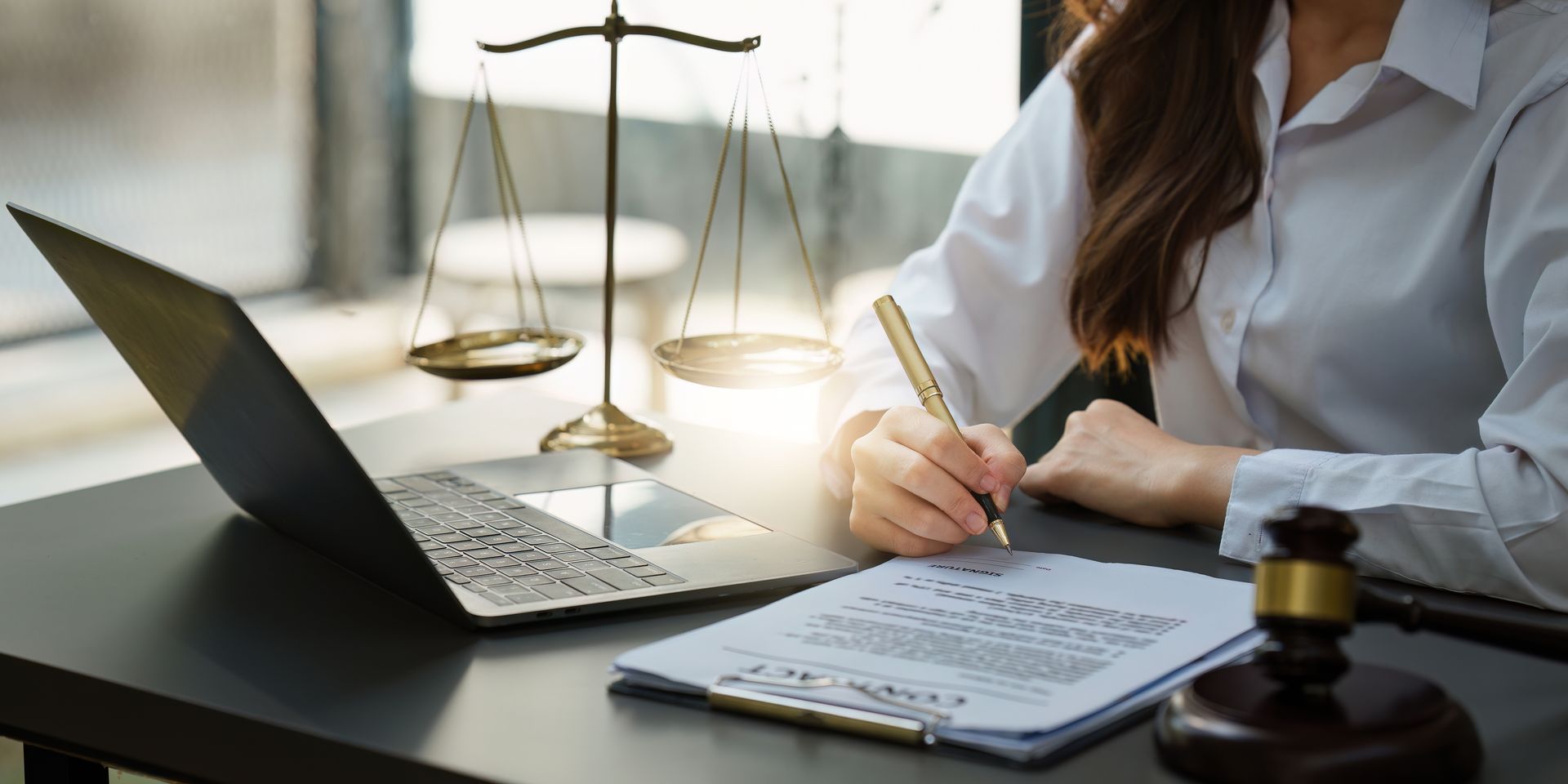 A woman is sitting at a desk with a laptop and a clipboard.
