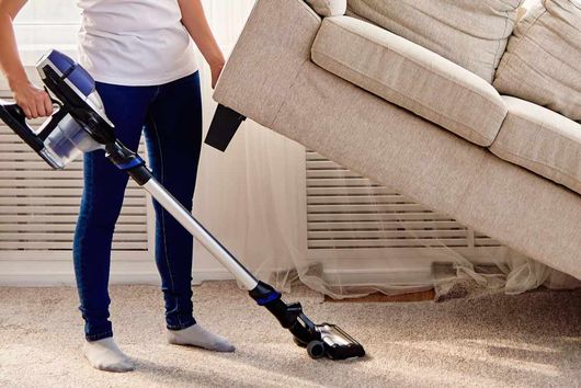 A cleaner lifting a sofa for thorough cleaning underneath