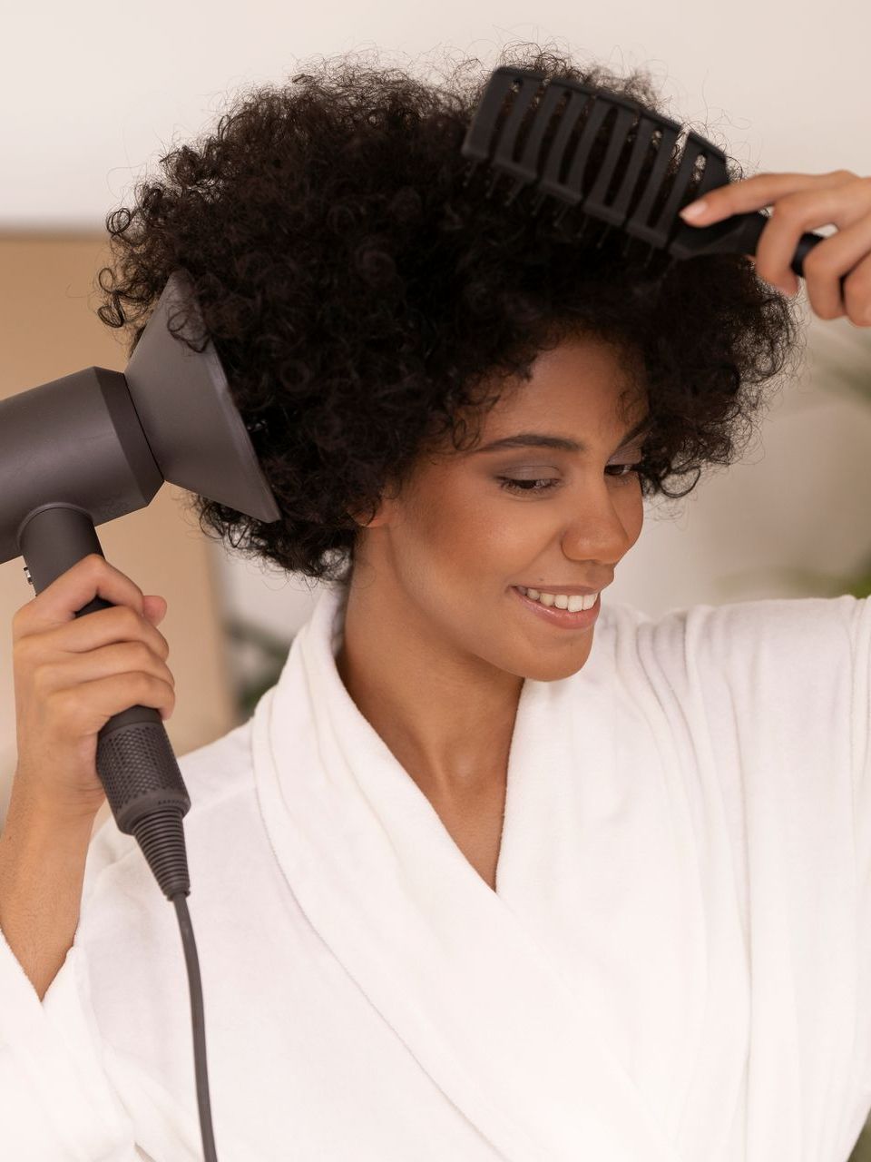 a woman in a white robe is blow drying her hair