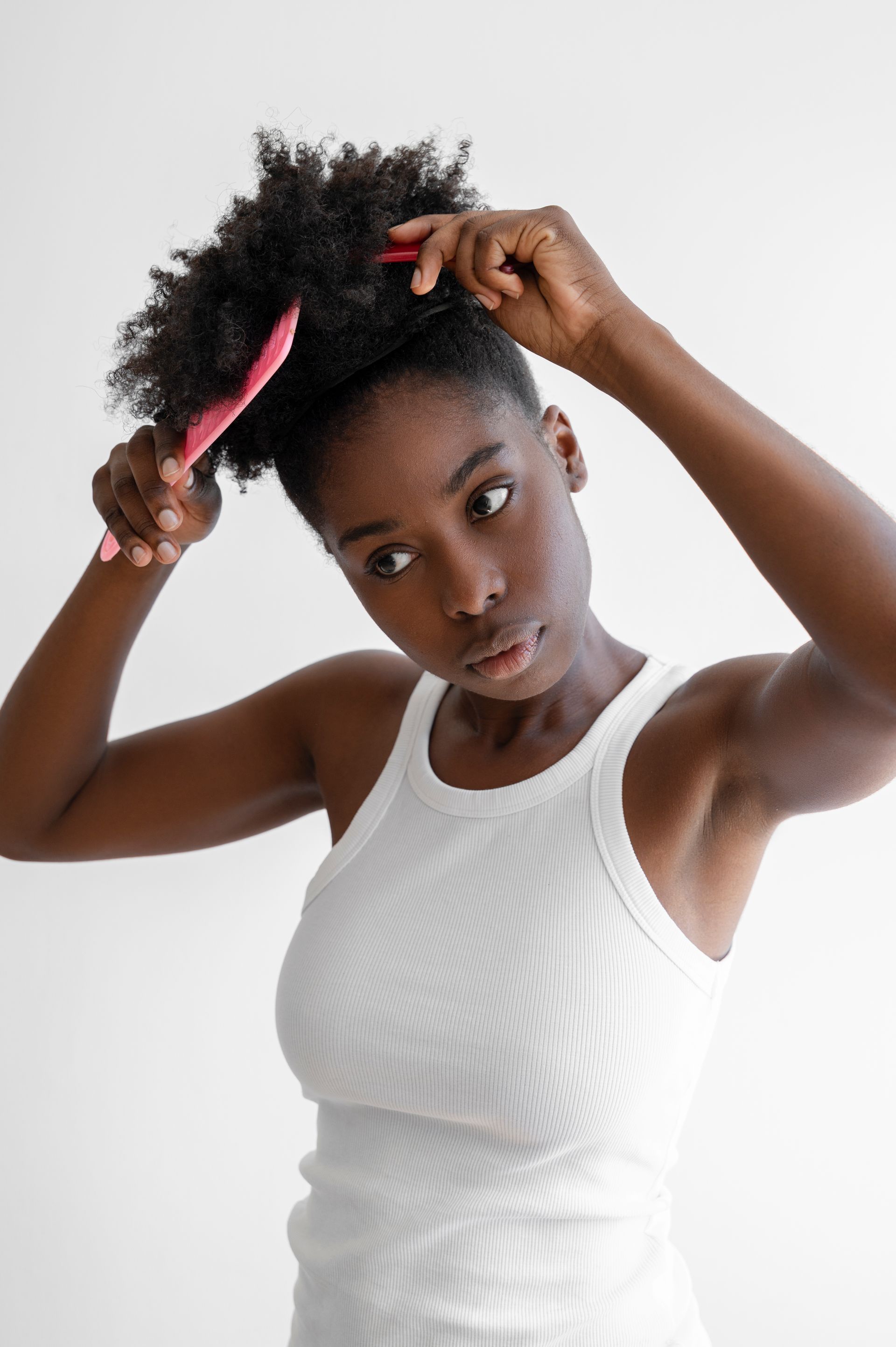 a woman in a white tank top is brushing her hair .