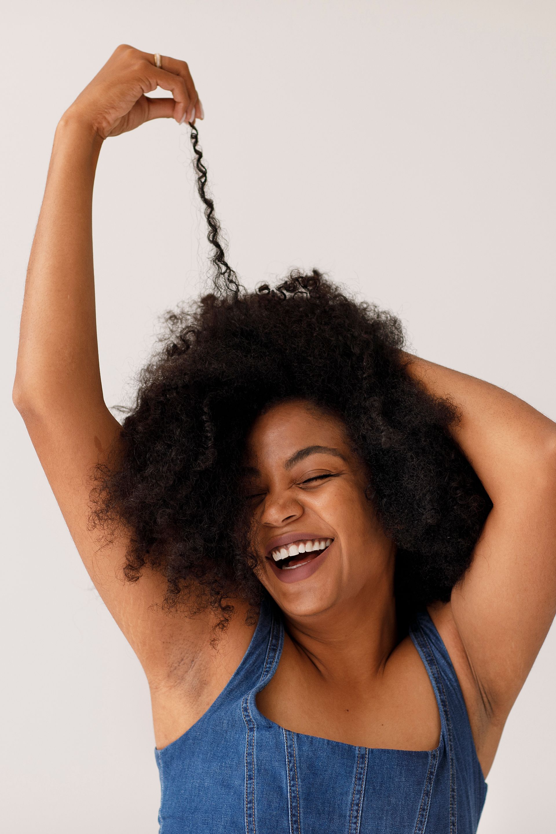 a woman with curly hair is smiling and holding her hair up in the air .