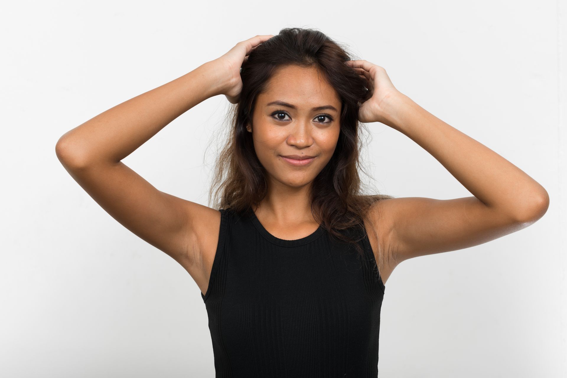 a woman in a black tank top is holding her hair in her hands .