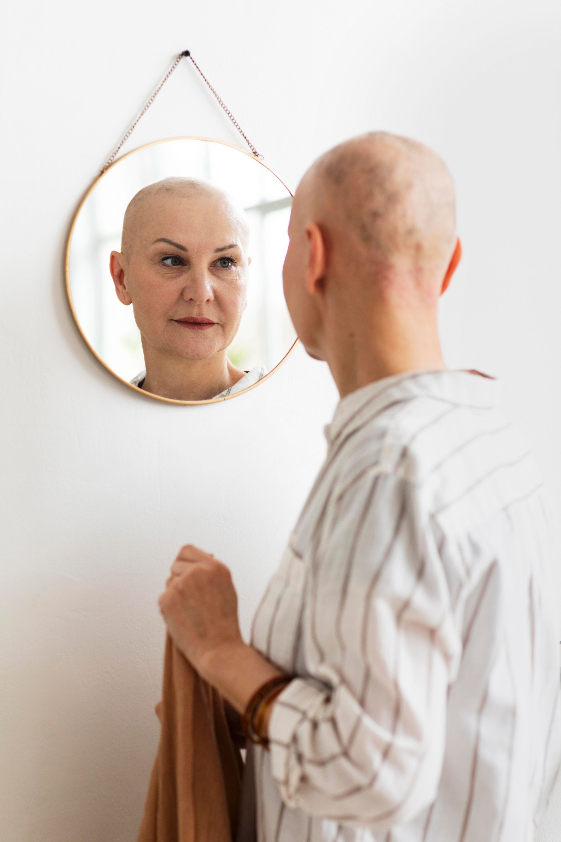 a bald woman looks at her reflection in a mirror