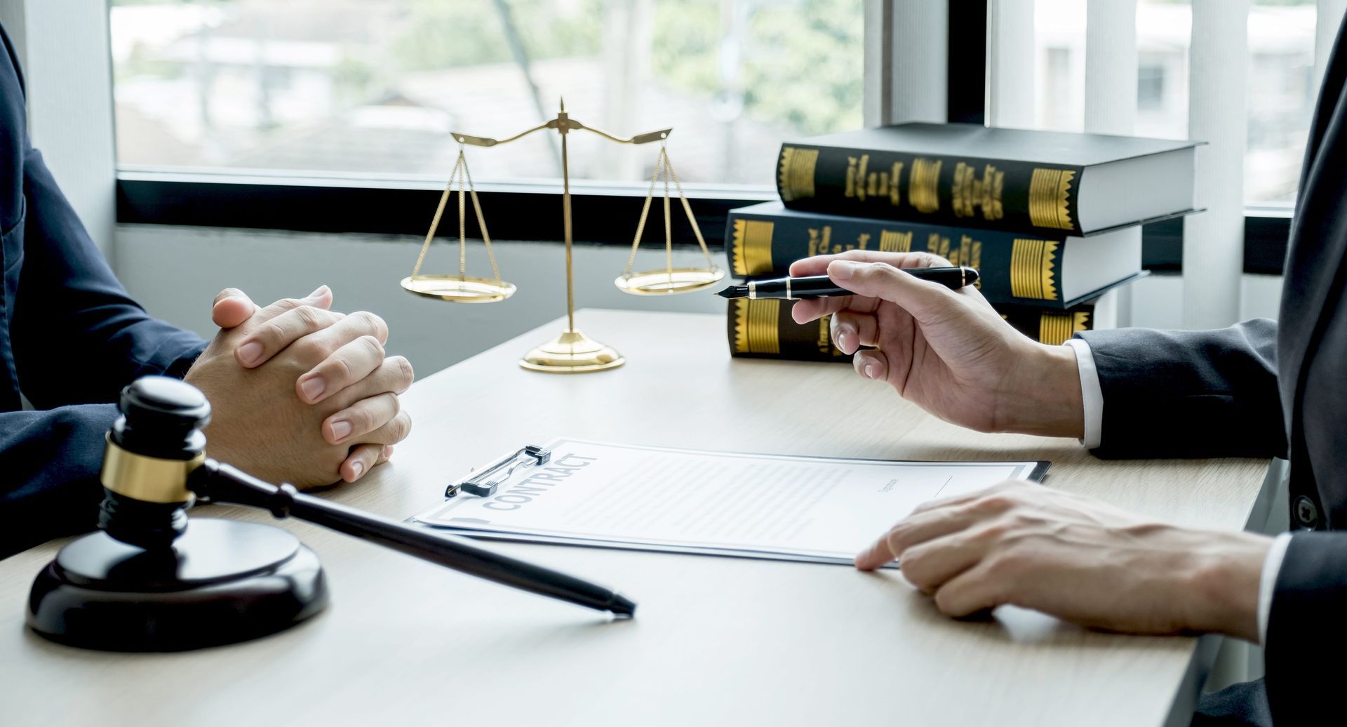 Law office meeting with gavel, legal books, scales, and people discussing a case across a desk