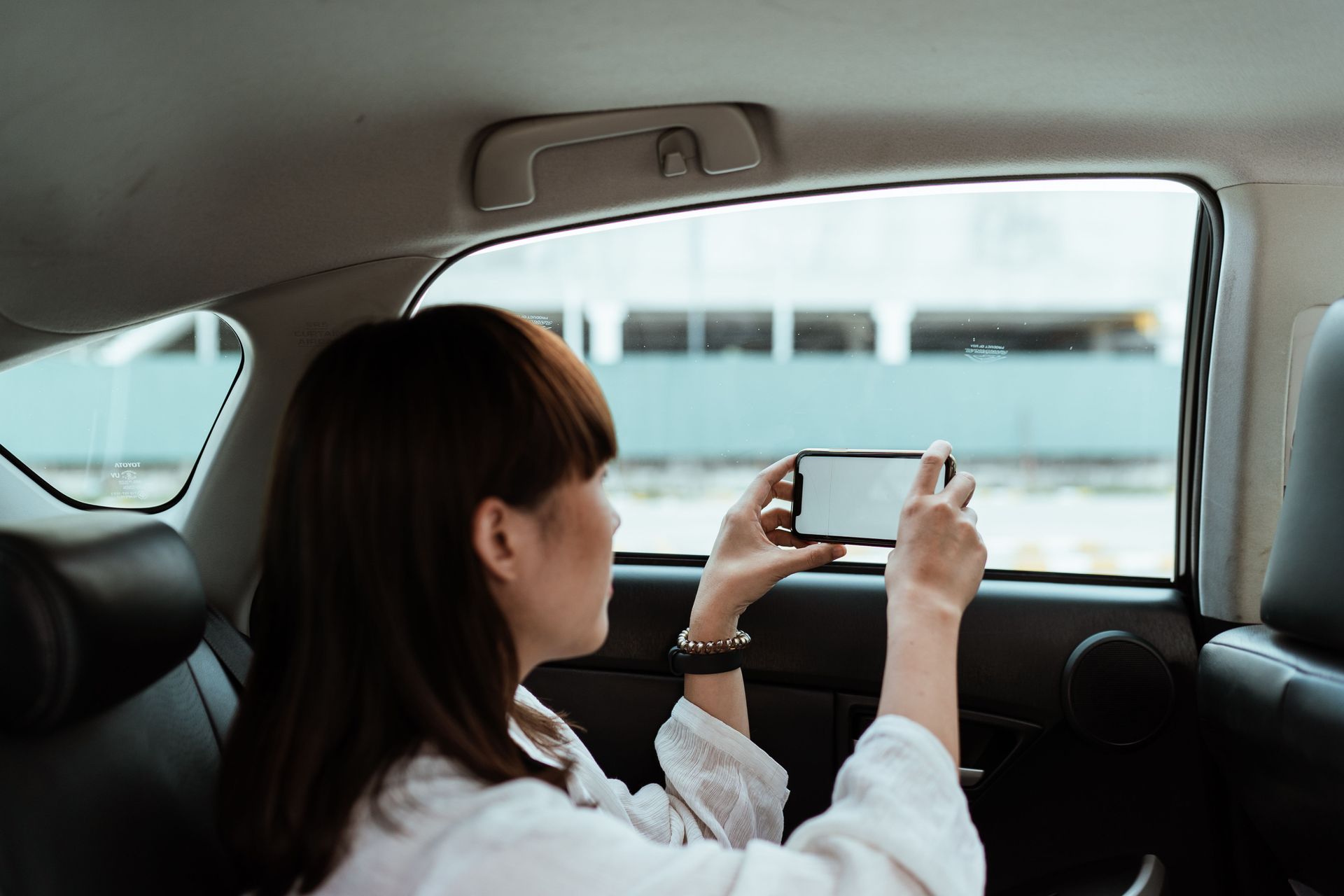 Person seated in a car taking a photo or video through the window with a smartphone