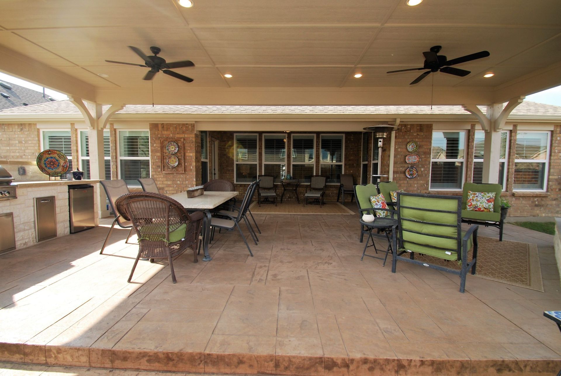 Patio with outdoor kitchen, dining table, chairs, and ceiling fans under a covered area.