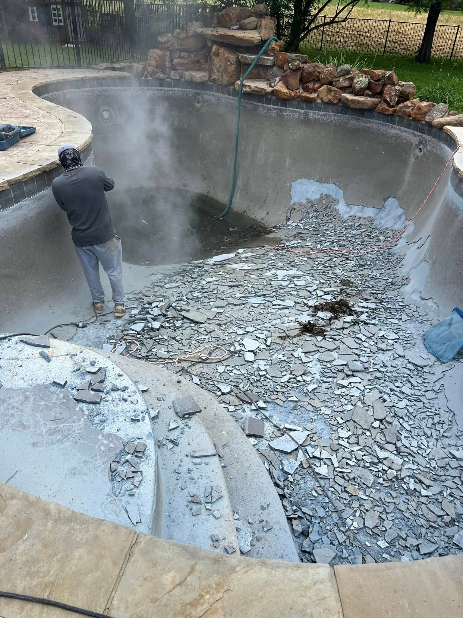 Man in pool removing tile debris from a drained pool.  Smoke rises in air.