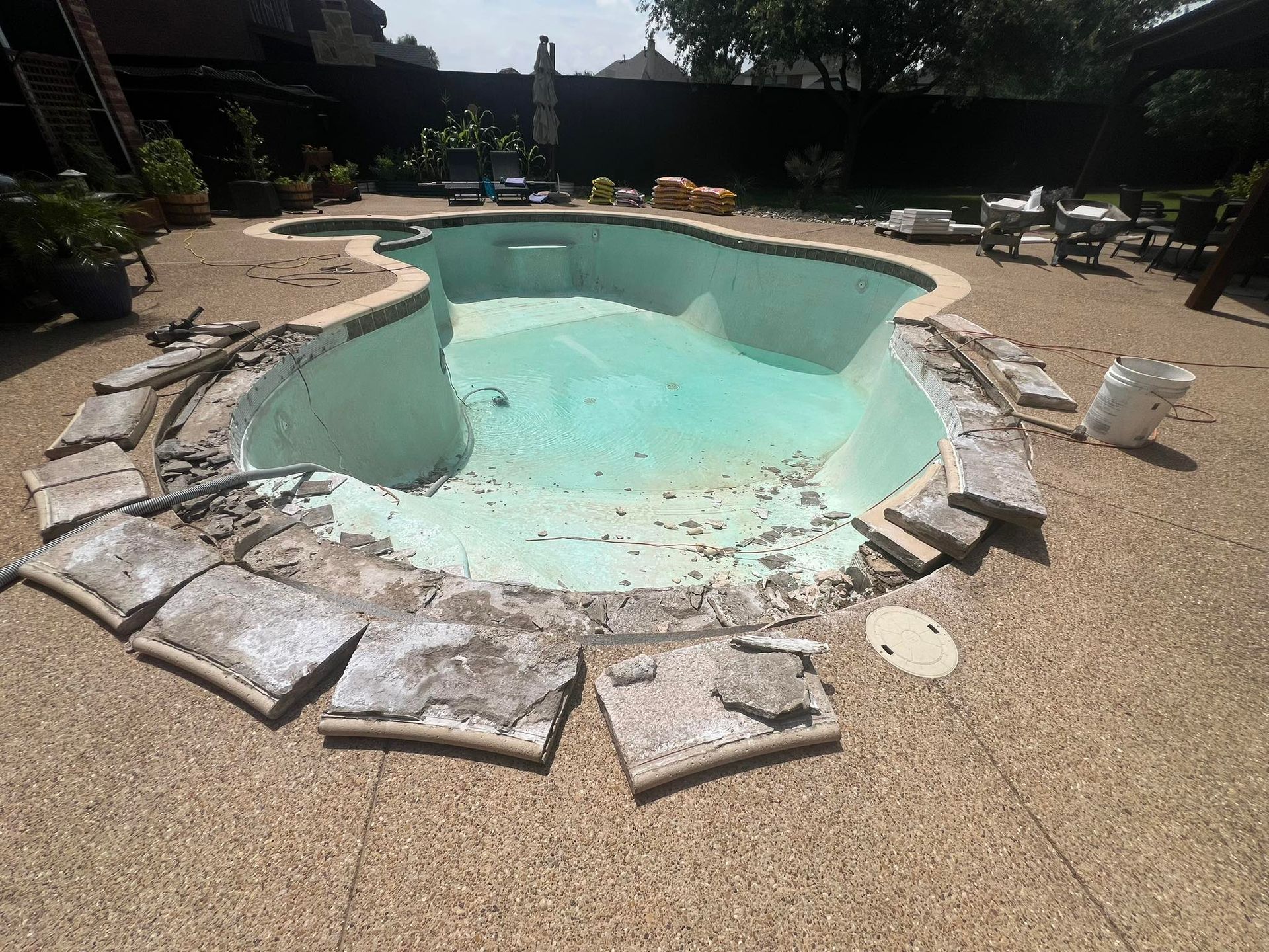 Pool undergoing renovation, surrounded by exposed concrete, debris, and work materials in an outdoor setting.
