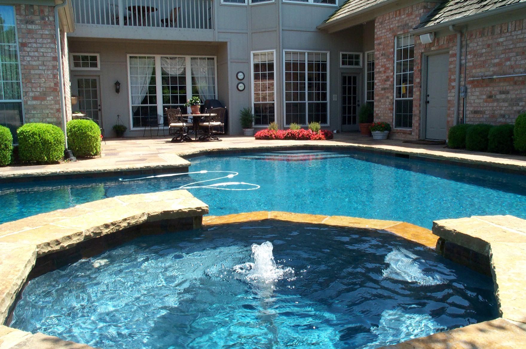 Backyard pool with a spa; blue water, stone surround, and house in background.