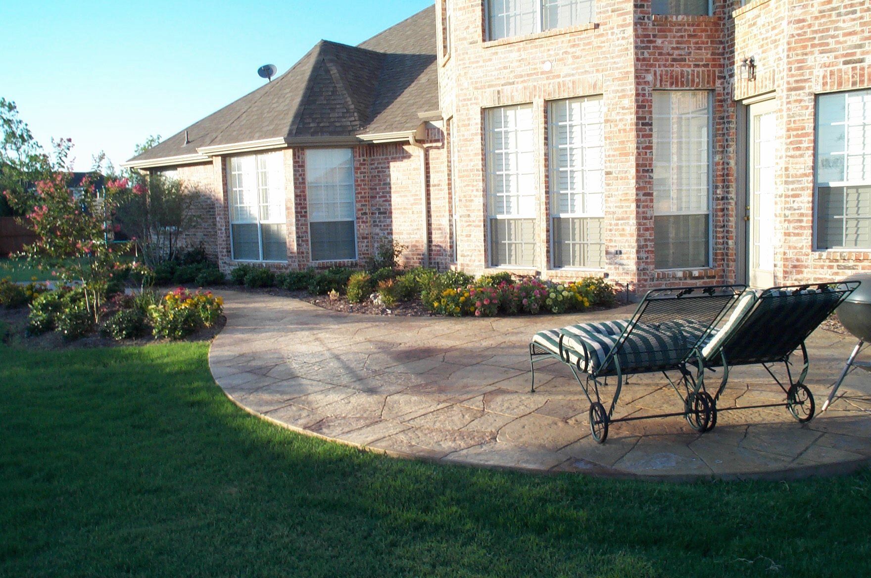 Brick house with stone patio, chaise lounges, and green lawn.