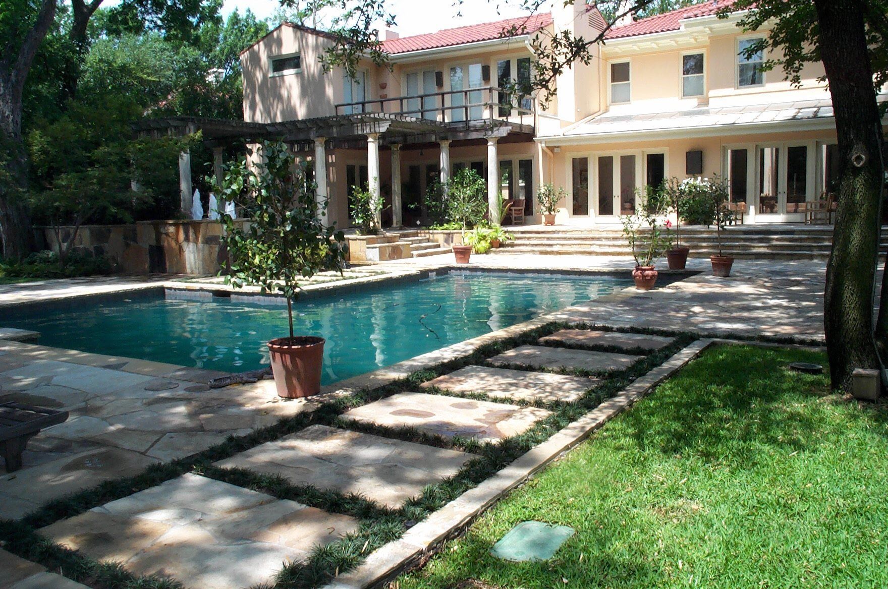 Backyard with pool, stone patio, and a large house with columns and balcony.