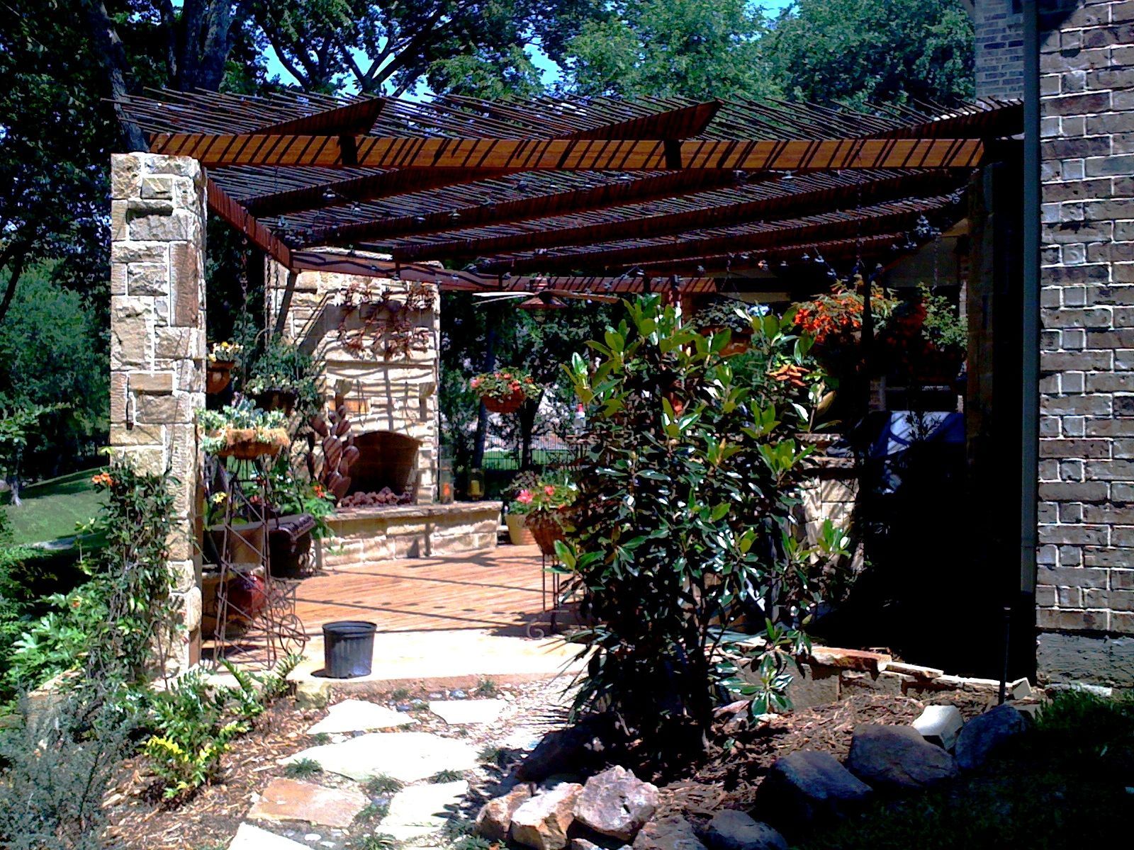 Stone patio with pergola, fireplace, plants, and hanging baskets.