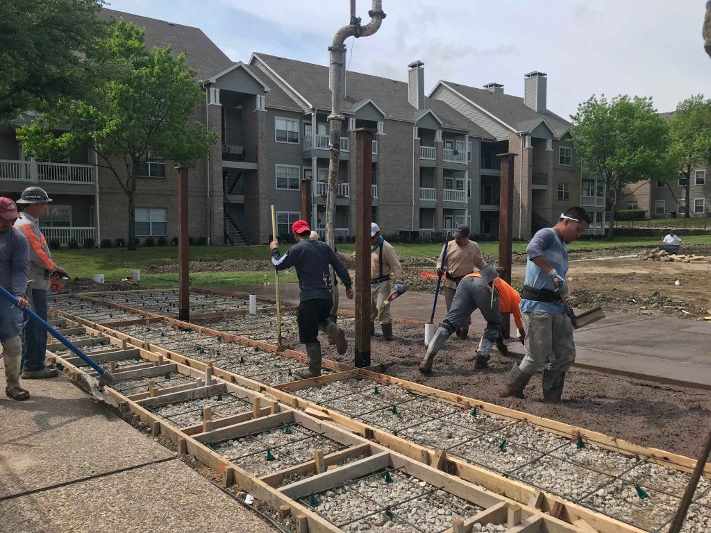 Construction workers pouring concrete for a walkway near an apartment building.