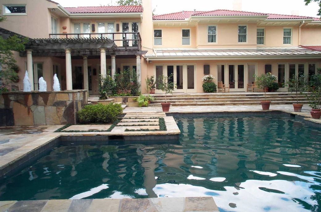 Swimming pool in front of a large peach-colored house with a balcony and columns.