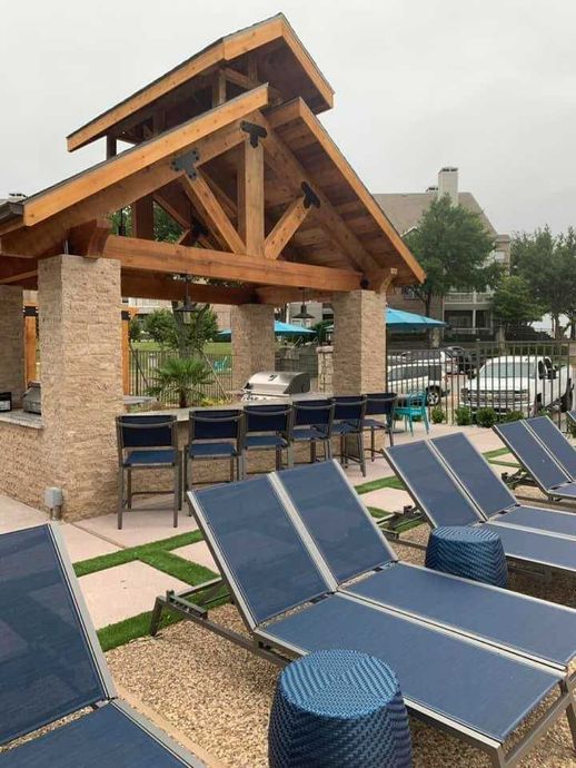 Poolside bar with lounge chairs. Blue chairs, stone columns, wooden beams.