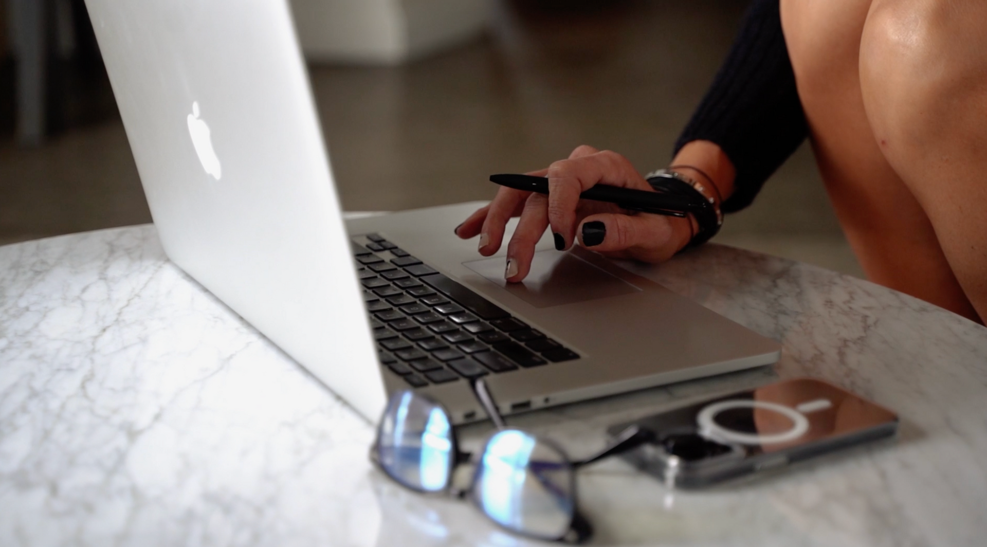 Person using a laptop on a table with glasses and a phone.
