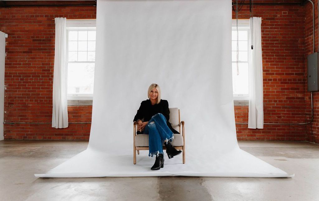 A woman is sitting in a chair in front of a white wall.