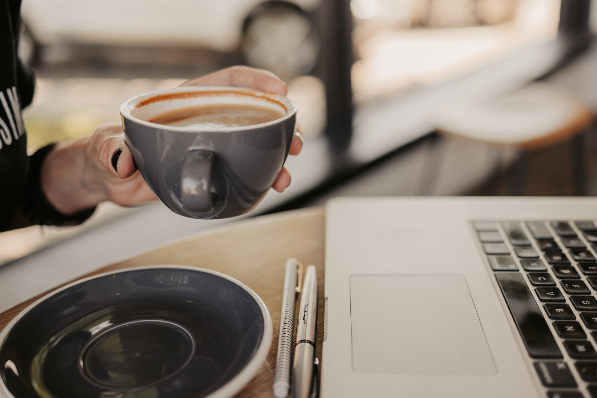 A person is holding a cup of coffee in front of a laptop.