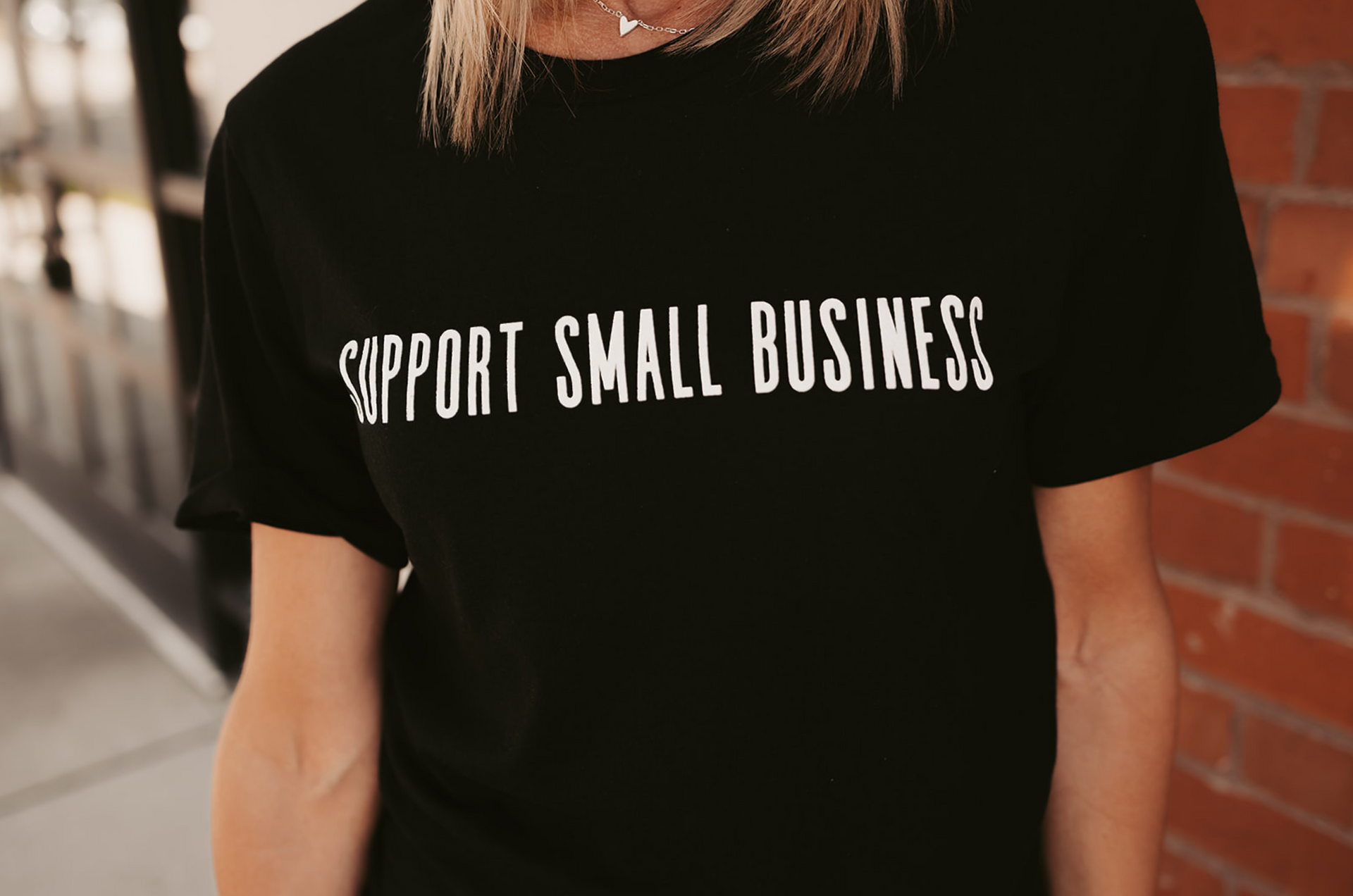 A woman is wearing a black t-shirt that says `` support small business ''.