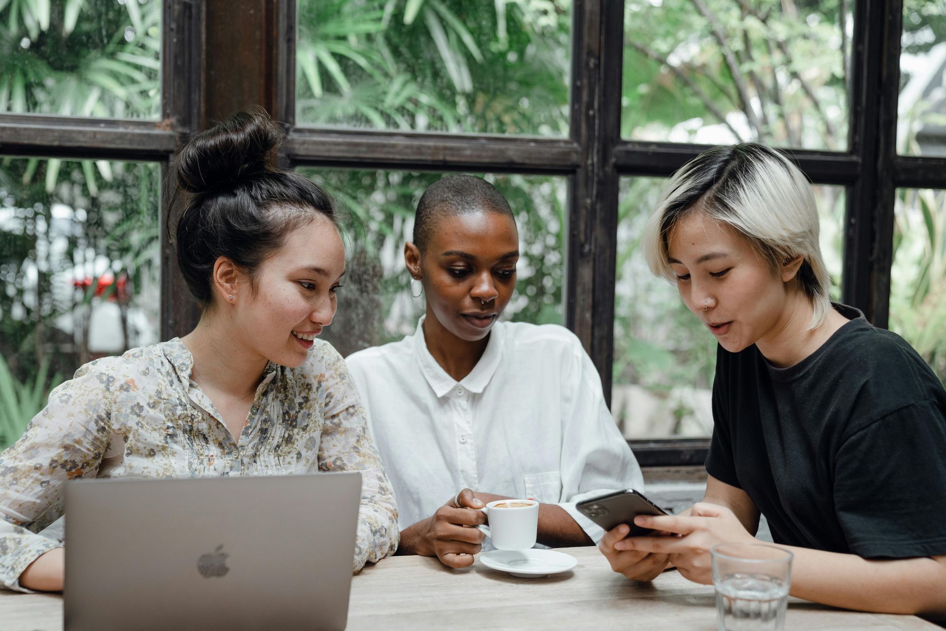 Three women are sitting at a table with a laptop and a cell phone.