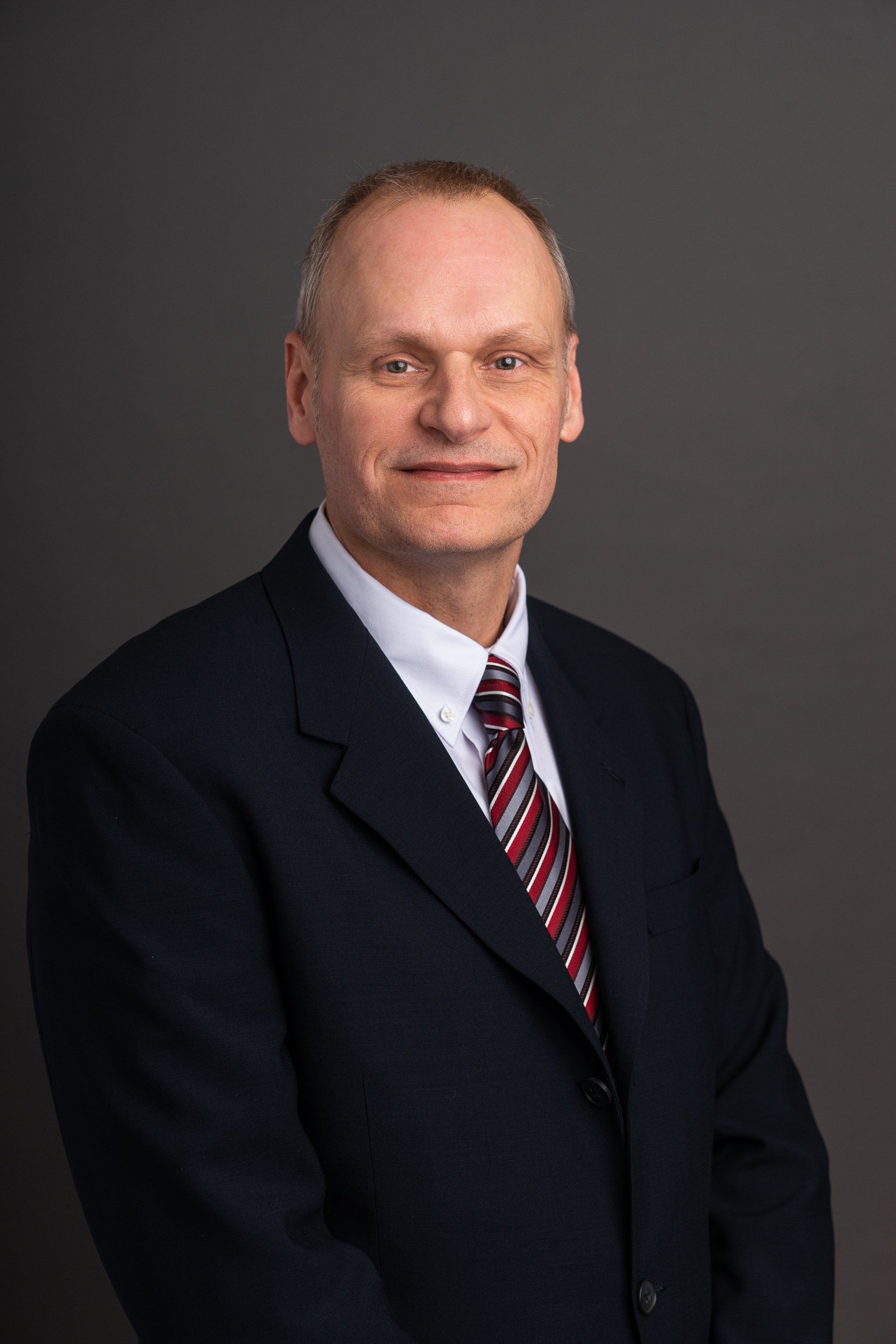 A man in a suit and tie is standing in front of a gray background.