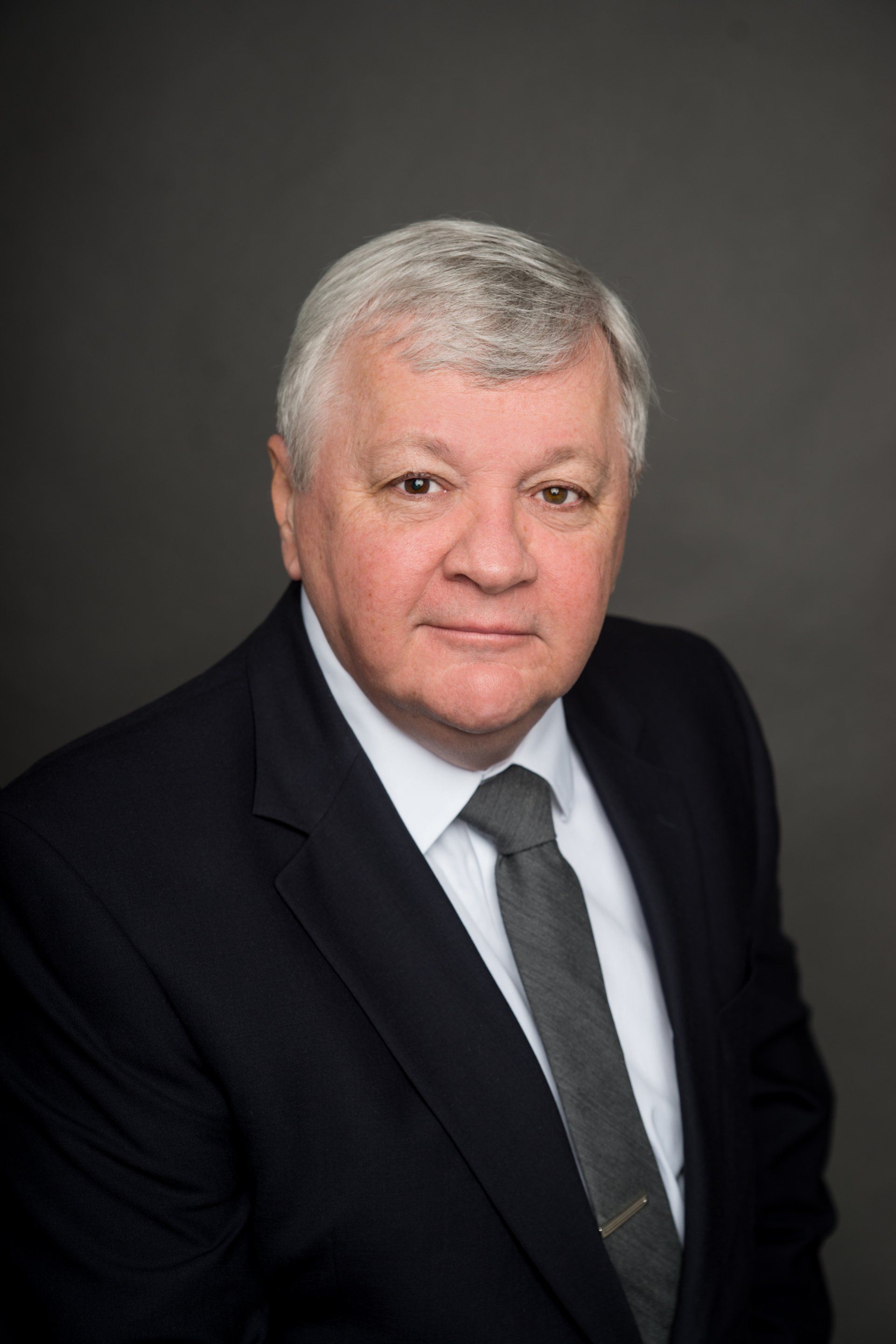 A man in a suit and tie is standing in front of a gray background.