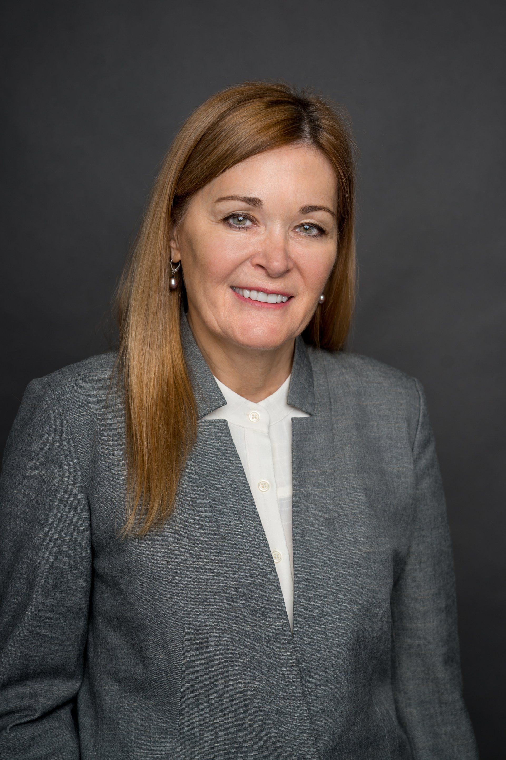 A woman in a gray suit and white shirt is smiling for the camera.
