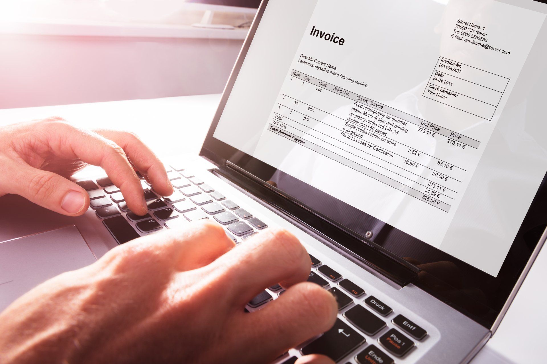 A person is typing an invoice on a laptop computer.