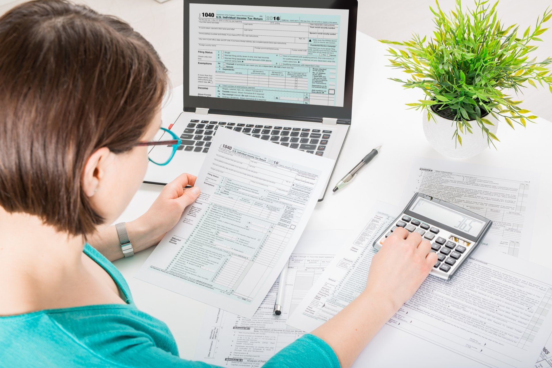 A woman is sitting at a desk with a laptop and a calculator.