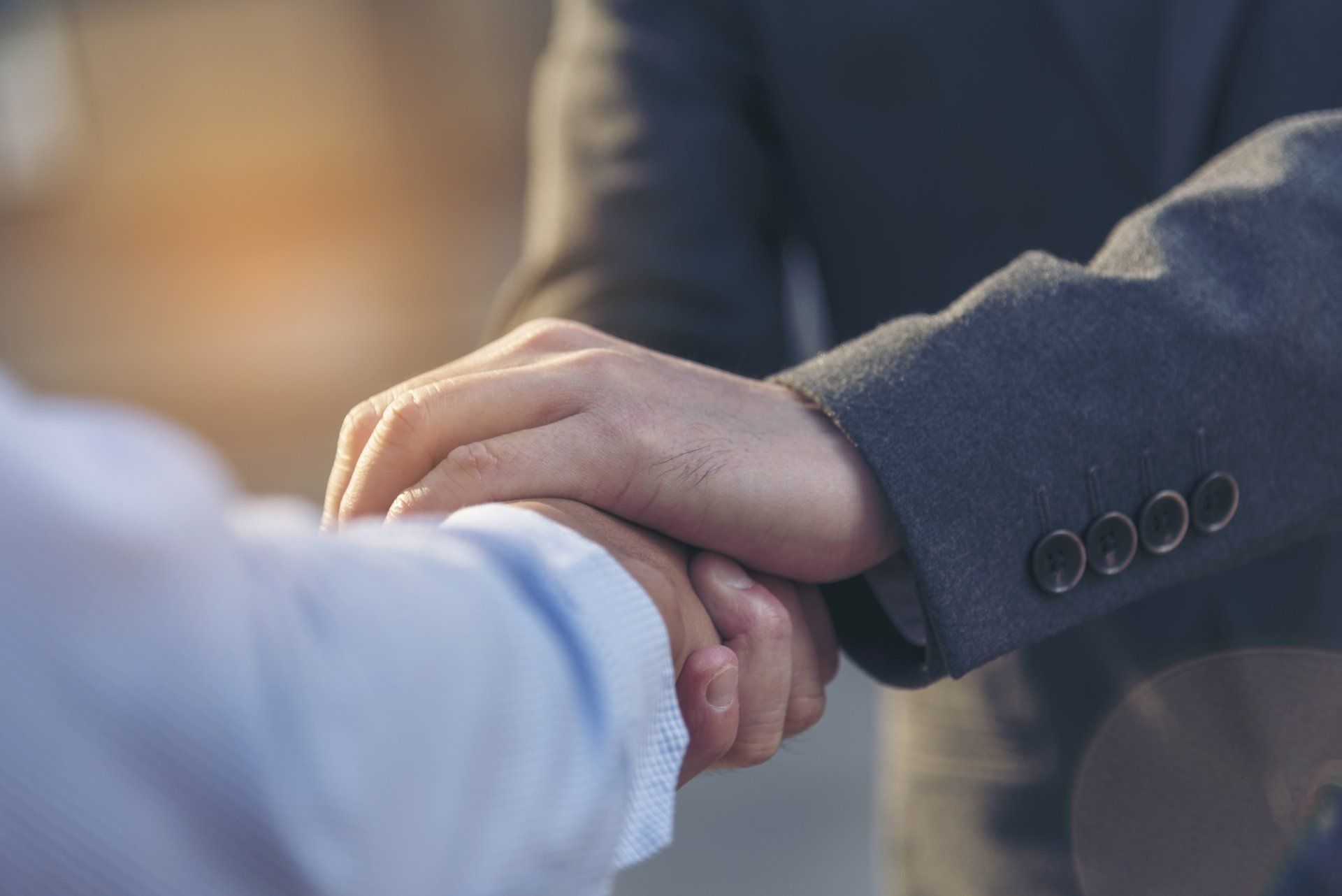 A man in a suit and a man in a blue shirt are shaking hands.