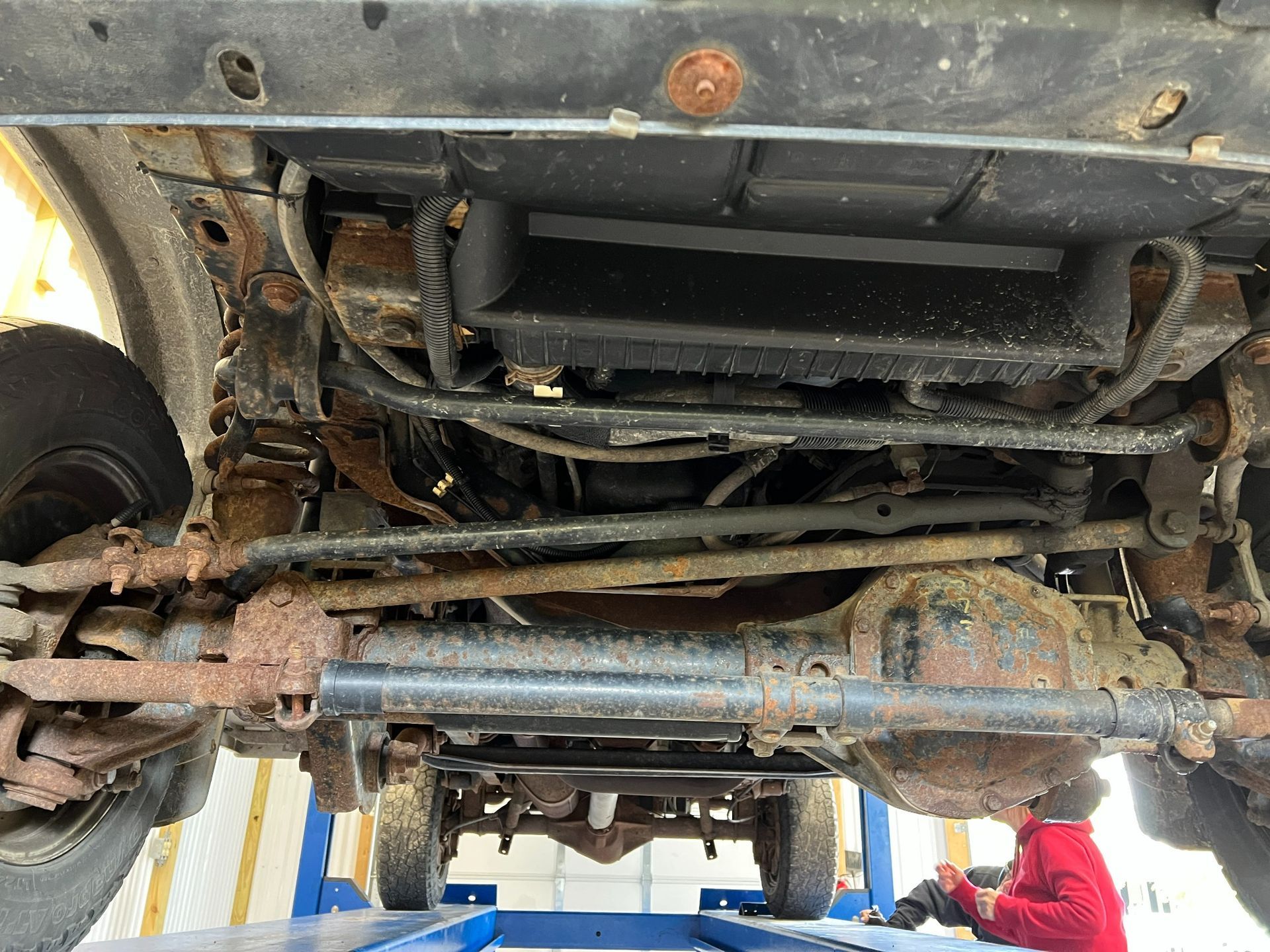 Undercarriage of a vehicle with axle, exhaust, and suspension components visible in a repair bay