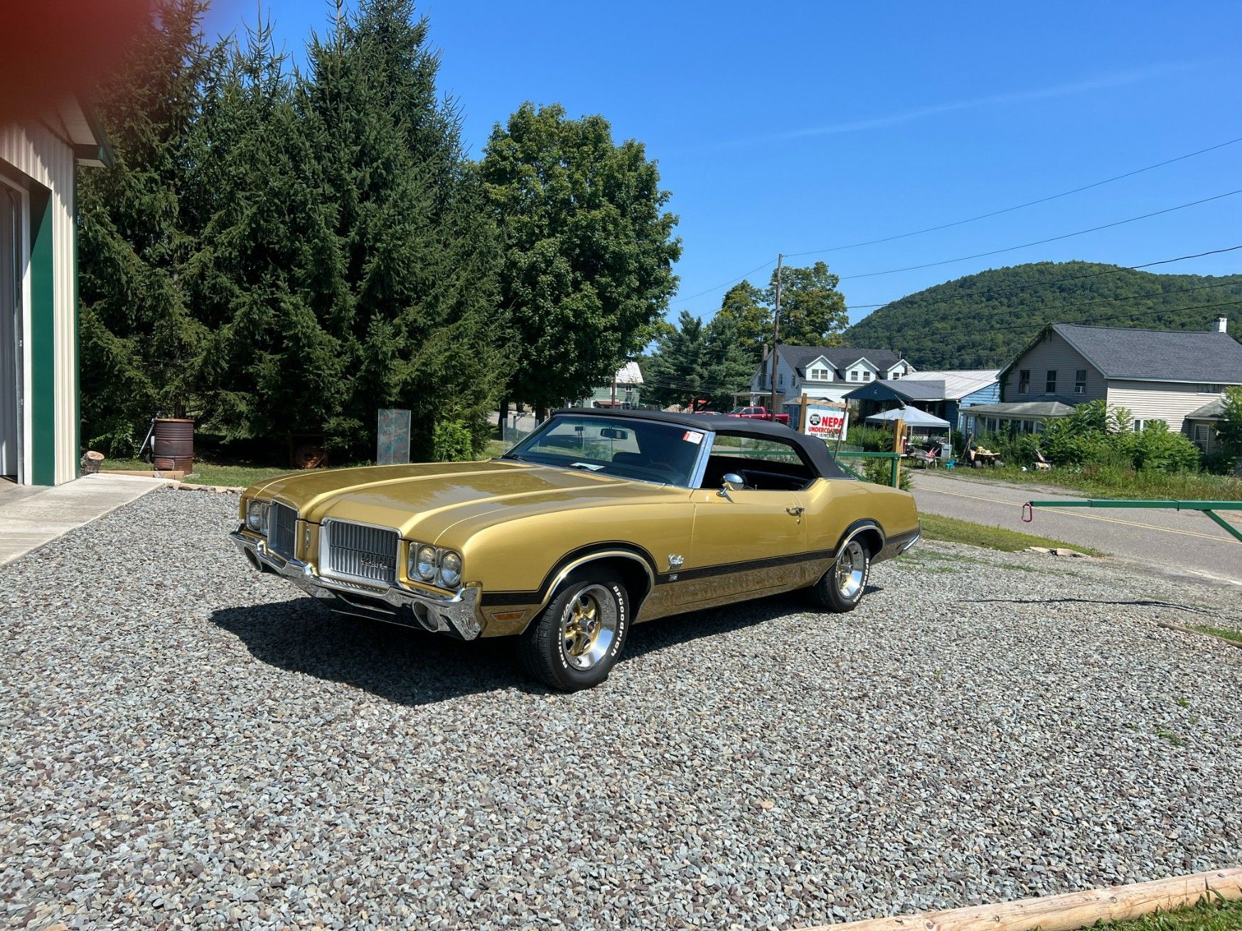 Gold classic convertible parked on gravel beside a building under a clear blue sky.
