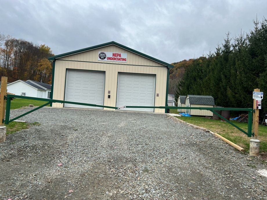 Gravel driveway leading to a beige garage with two white doors and green fencing on a cloudy day