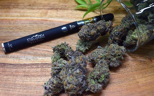 A vape pen and cannabis buds on a wooden surface.