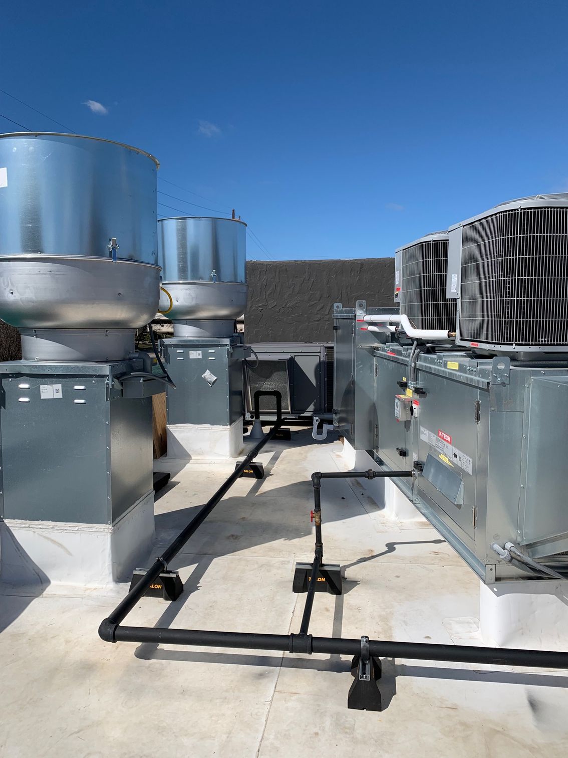 Rooftop HVAC units on a white surface, blue sky above. Black pipes run between the units.