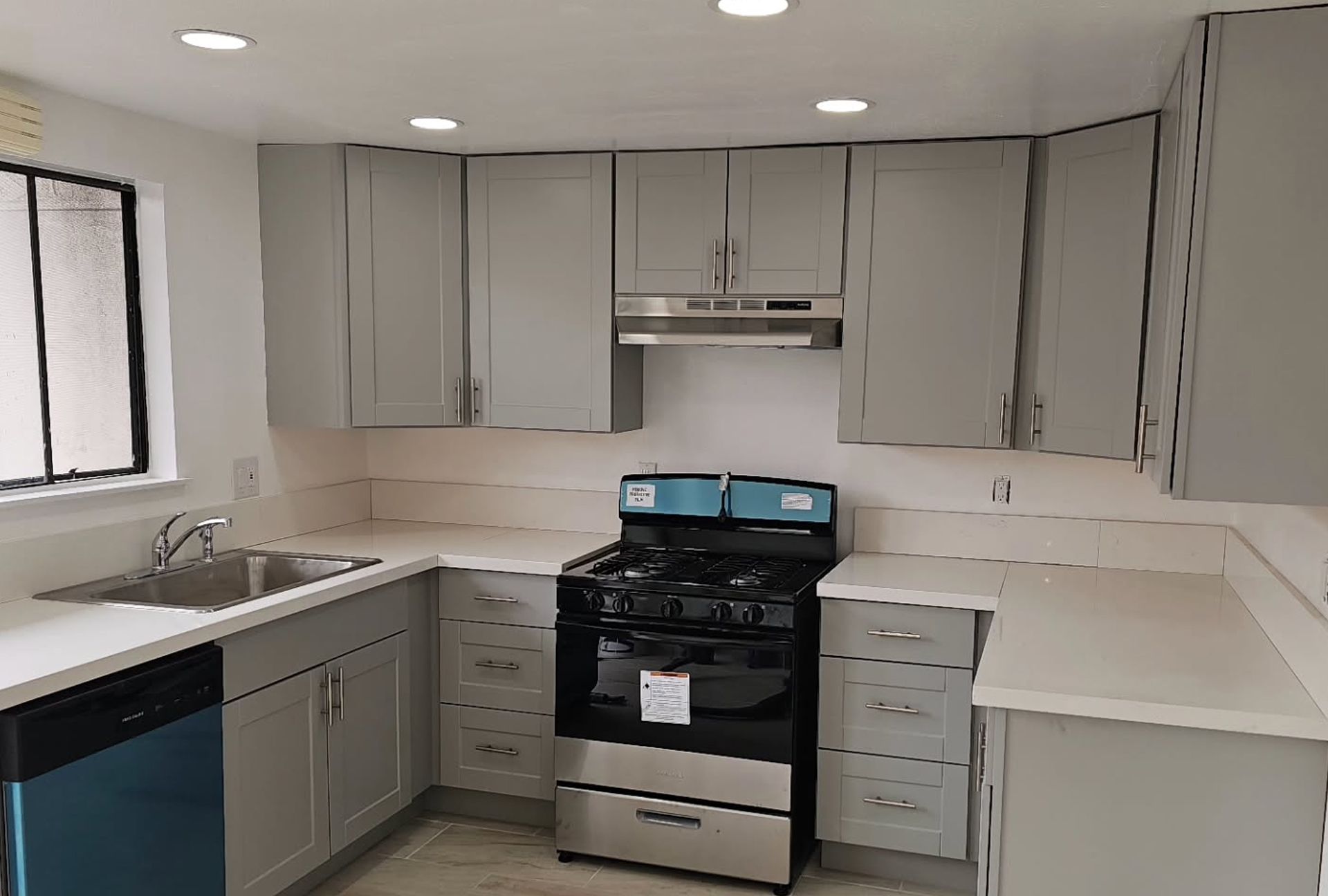 Gray kitchen with white countertops, stainless steel stove, and blue dishwasher.