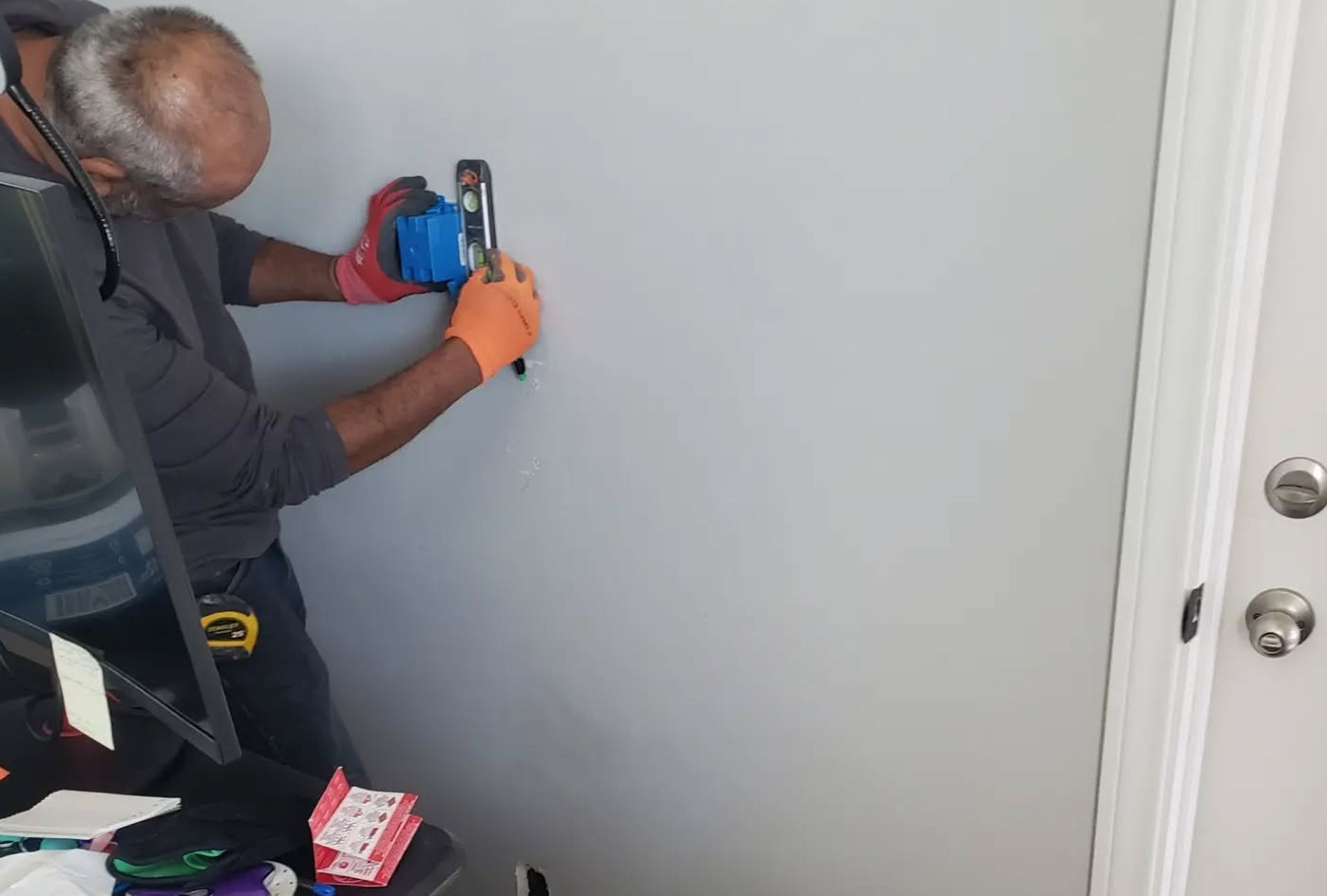 Person using tools on a wall, wearing gloves. Next to a door.