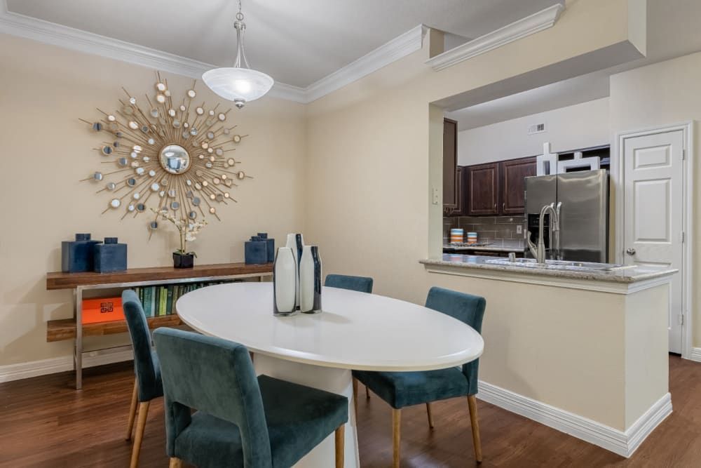 a dining room with a table and chairs and a kitchen in the background at Marquis at Kingwood in Kingwood, TX.