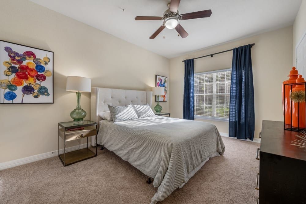 a bedroom with a bed, nightstand, dresser, and ceiling fan at Marquis at Kingwood in Kingwood, TX.