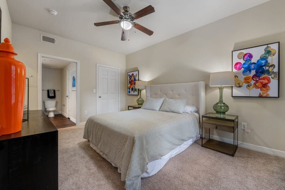 a bedroom with a bed, a ceiling fan, a dresser, and a toilet at Marquis at Kingwood in Kingwood, TX.
