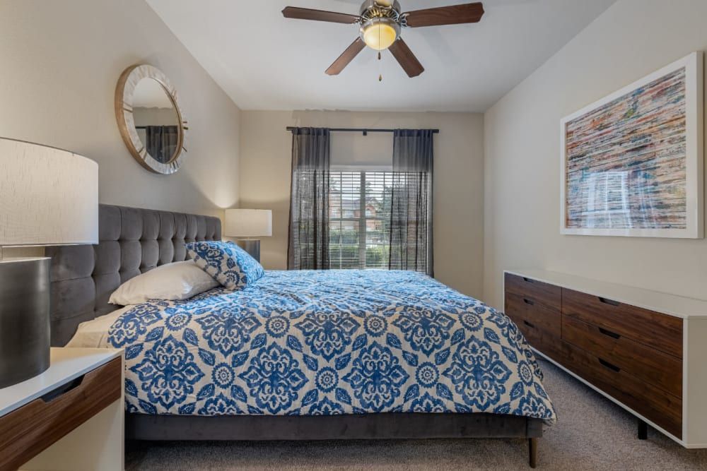 a bedroom with a bed, dresser, mirror, and ceiling fan at Marquis at Kingwood in Kingwood, TX.