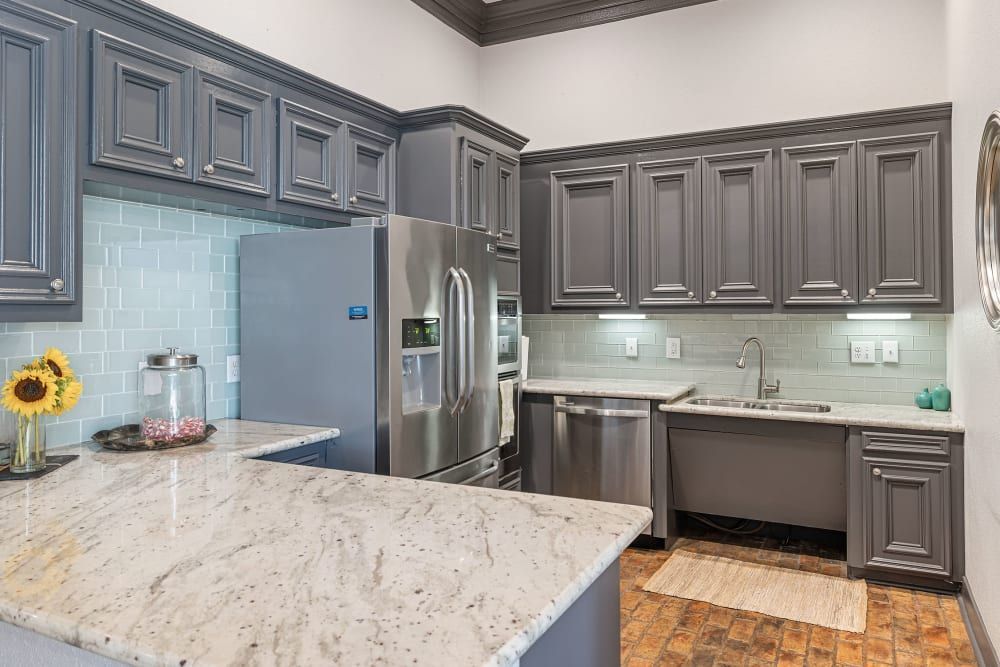 a kitchen with gray cabinets, granite counter tops, stainless steel appliances, and a large island at Marquis at Kingwood in Kingwood, TX.