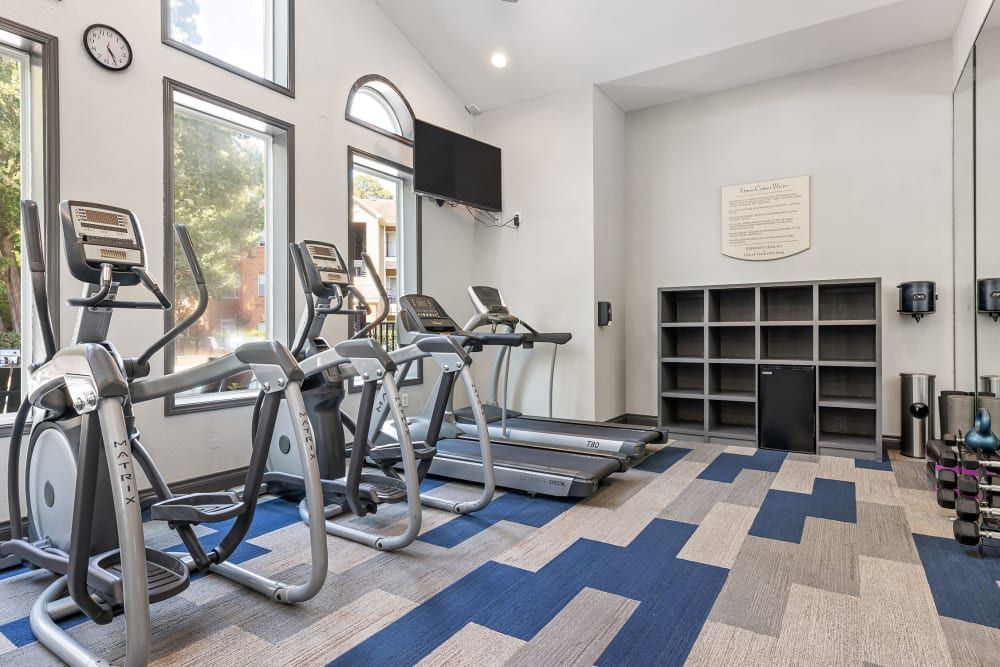 a gym with treadmills, ellipticals, and a large mirror at Marquis at Kingwood in Kingwood, TX.