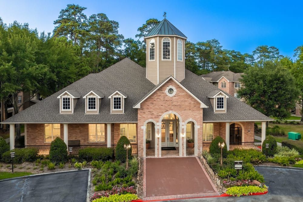 a large brick building with a tower on top of it is surrounded by trees at Marquis at Kingwood in Kingwood, TX.