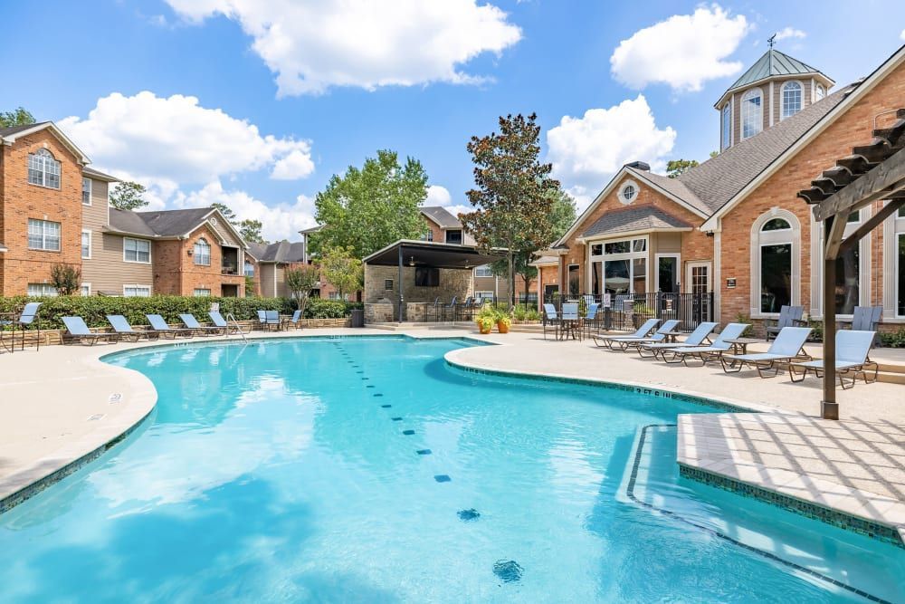 a large swimming pool surrounded by chairs in front of a brick building at Marquis at Kingwood in Kingwood, TX.